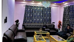 A modern living room with a black leather sofa, two wooden coffee tables, and patterned curtains. - Hotel Golden Eye (Srinagar)