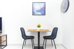 Uma sala de jantar moderna com mesa de madeira, duas cadeiras pretas, um vaso com planta e um quadro de paisagem na parede.