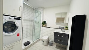Un baño moderno con lavadora, cabina de ducha de vidrio, inodoro e lavamanos con espejo.