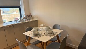 Un comedor con una mesa preparada para cuatro personas, incluyendo platos, tazones, cubiertos y copas de vino.