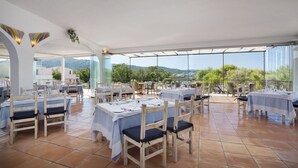 Un área de comedor al aire libre con varias mesas y sillas, una vista despejada del paisaje circundante y una sección cubierta con techo de vidrio.
