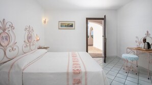 Un dormitorio con cama, escritorio, silla, un cuadro en la pared y una puerta abierta que da a otra habitación.