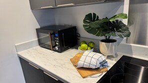 A kitchen with a microwave, a plant, a bowl of limes, and a loaf of bread on a marble countertop. - Quiet 1-Bed Apartment in Swindon Old Town (Swindon)