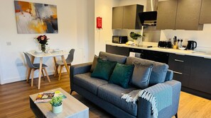 A modern living room with a grey sofa, a coffee table with a plant, and a dining area with a white table and chairs. - Quiet 1-Bed Apartment in Swindon Old Town (Swindon)