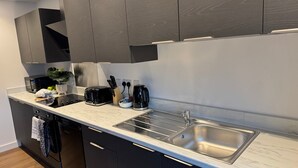 Uma cozinha moderna com armários escuros, bancada de mármore, forno embutido, torradeira, cafeteira e pia.