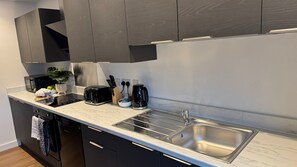 A modern kitchen with dark cabinetry, a marble countertop, a built-in oven, a toaster, a coffee maker, and a sink. - Quiet 1-Bed Apartment in Swindon Old Town (Swindon)