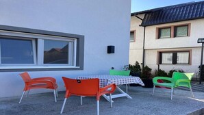An outdoor patio with a table and chairs, a window, and a building in the background.