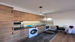 A modern kitchen with wooden cabinets, a built-in washing machine, and a dining area with a table and chairs.