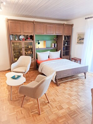 A bedroom with a bed, two chairs, a small table, wooden cabinets, and a green wall. - Monte e Mare Apartment – Your Black Forest Retreat with Baltic Sea Charm (Todtnauberg)