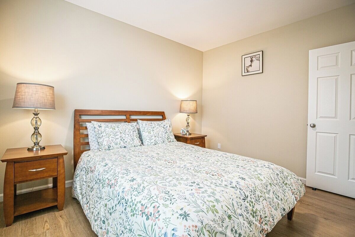 Un dormitorio con cama, dos mesitas de noche, una mesilla auxiliar, una puerta y un cuadro colgado en la pared.