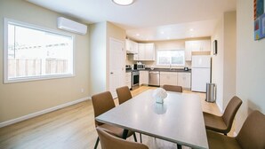 Een moderne keuken met witte kasten, een eettafel met stoelen en een raam met jaloezieën.