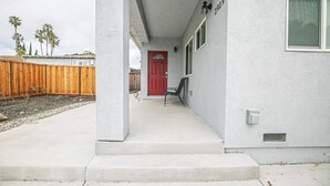 Een huis met een rode deur, een houten omheining en een betonnen veranda.