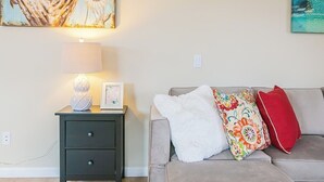 Een woonkamer met een bank, een bijzettafeltje met een lamp en twee schilderijen aan de muur.