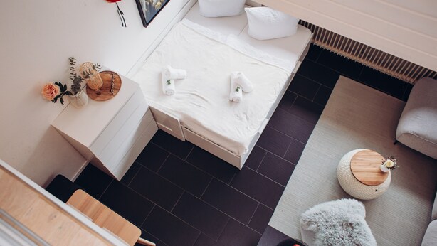 Une chambre d’hôtel moderne, équipée d’un lit, d’un petit bureau, d’une table d’appoint ronde en bois et d’un canapé gris.