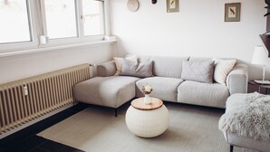 Un salon moderne avec un canapé d’angle, une table basse ronde et un radiateur.