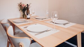 Une table à manger dressée avec des assiettes, des couverts, des verres à vin et une bouteille de vin, entourée de chaises.
