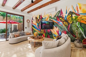 Ein modernes Wohnzimmer mit einer großen, farbenfrohen Wandmalerei von einem Schmetterling, einem Sofa, einem Couchtisch und einer Topfpflanze.