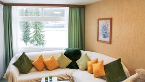 A hotel room with a large bed, green curtains, a framed picture on the wall, and a window with a view of trees. - Apartment Schwarzwald-Kult – Your Retro Time Travel Experience (Schluchsee)
