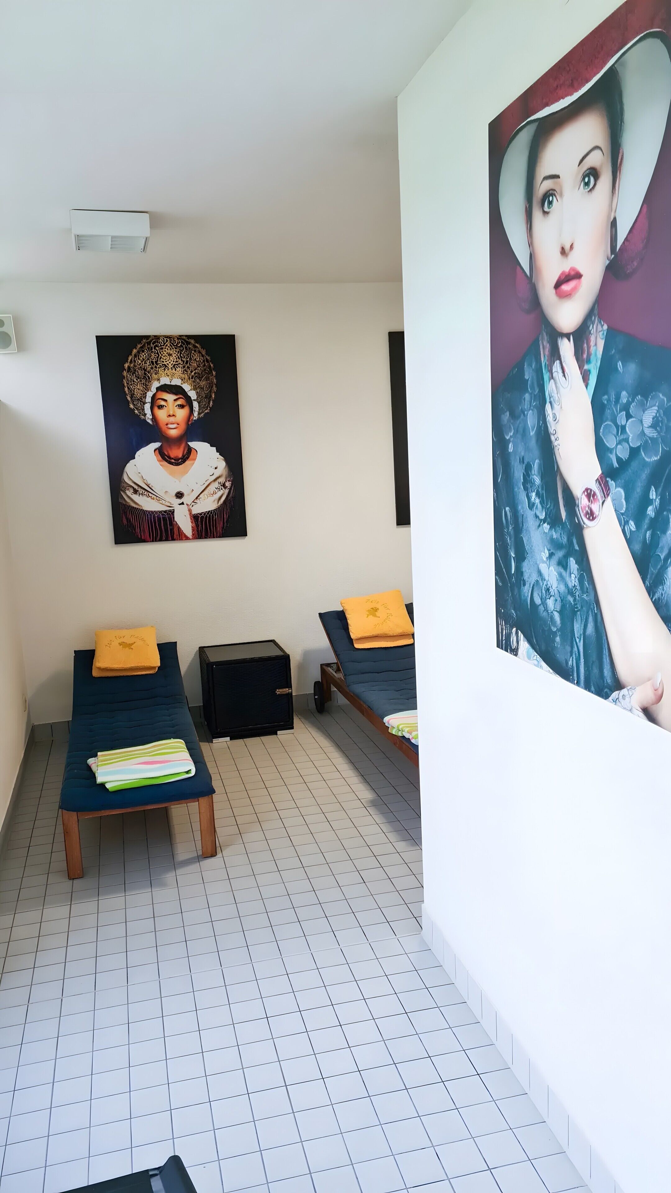 Ein Zimmer mit zwei Betten, einer Bank, einem Wandbild und einem kleinen schwarzen Schrank.