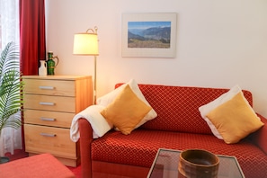 Un sofá rojo con cojines estampados, una mesita de madera, una lámpara, un cuadro en la pared y una planta.