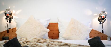 A bed with white pillows and a wooden headboard, two wall-mounted light fixtures, and a power outlet on the floor.