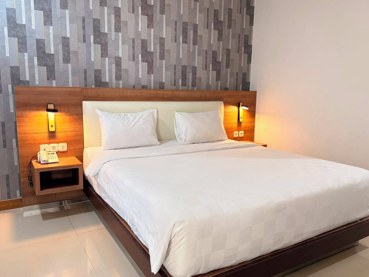 A hotel room with a large bed, two bedside tables with lamps, and a modern patterned wall.