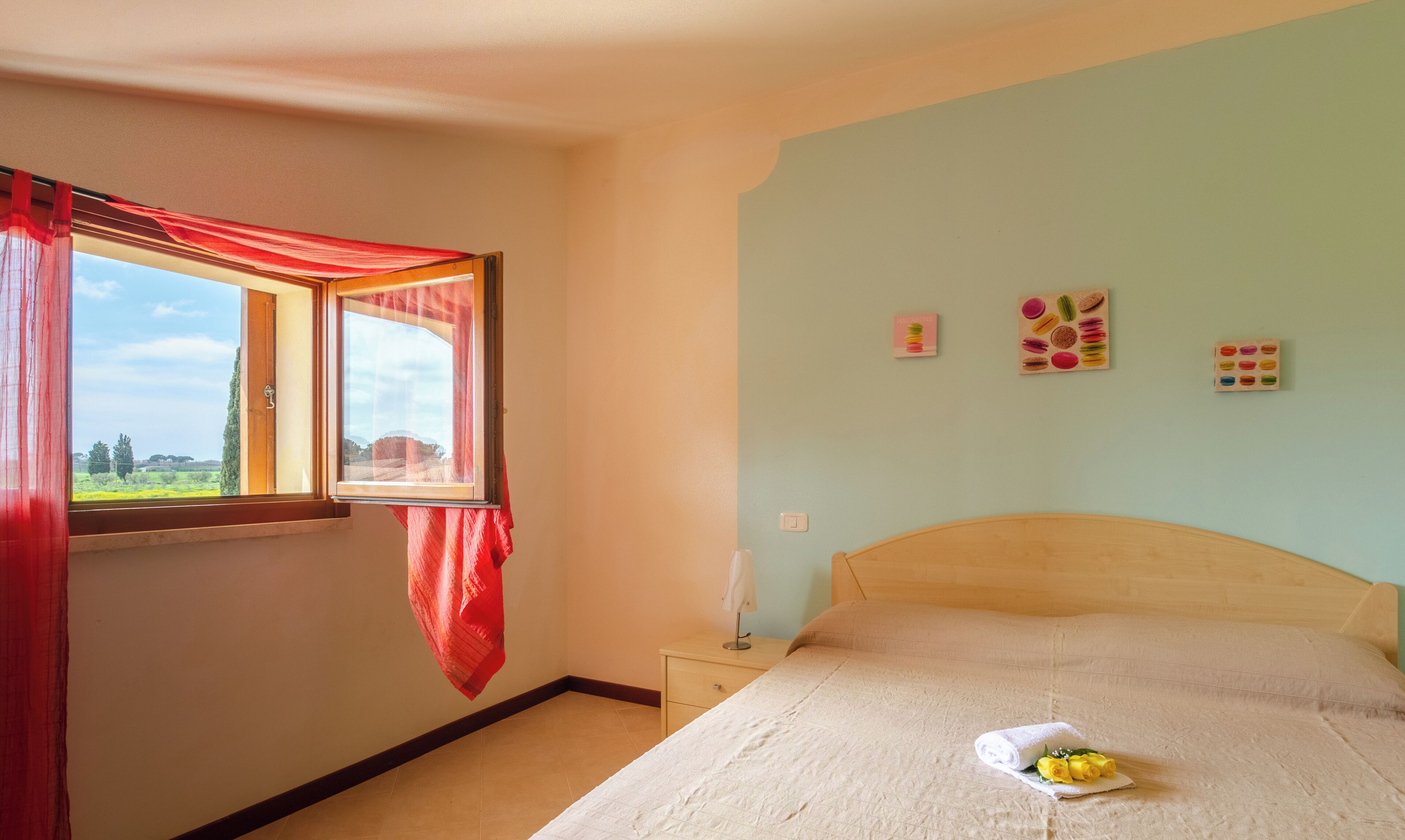 A bedroom with a bed, a nightstand, a window with red curtains, and wall decorations.