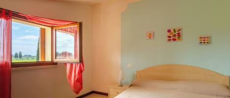 A bedroom with a bed, a nightstand, a window with red curtains, and wall decorations.
