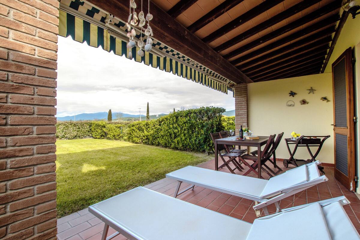 A patio with a table and chairs, a white bench, and a view of the garden and mountains.