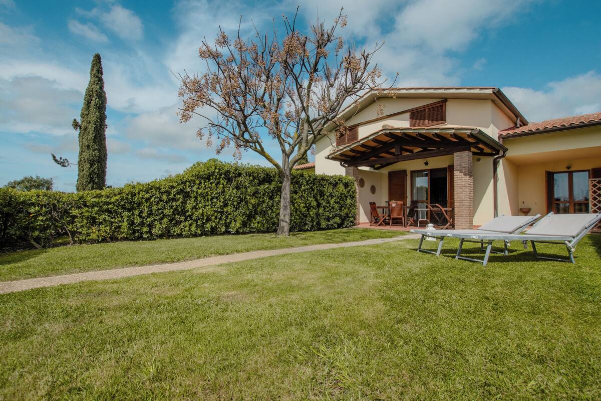 A house with a covered patio, a lawn, and a tree.