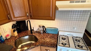Una cocina con armarios de madera, encimera de granito, un fregadero, un tostador y una estufa.