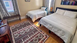 Un dormitorio con dos camas, un tapete estampado, un cuadro de un paisaje urbano y un equipo de aire acondicionado.