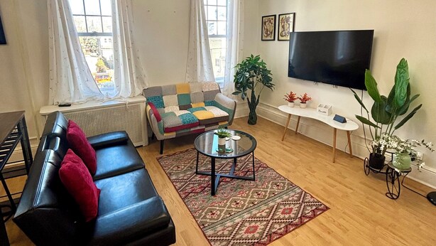 Una sala de estar con un sofá negro, un sillón estampado, una mesa de centro y un televisor.