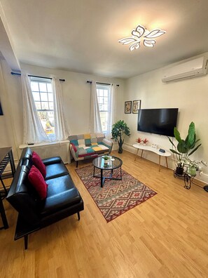 Una sala de estar con un sofá negro, un sillón estampado, una mesa de centro y un televisor.