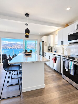 Une cuisine moderne dotée d’un grand îlot central, d’appareils électroménagers en acier inoxydable et offrant une vue sur la mer.