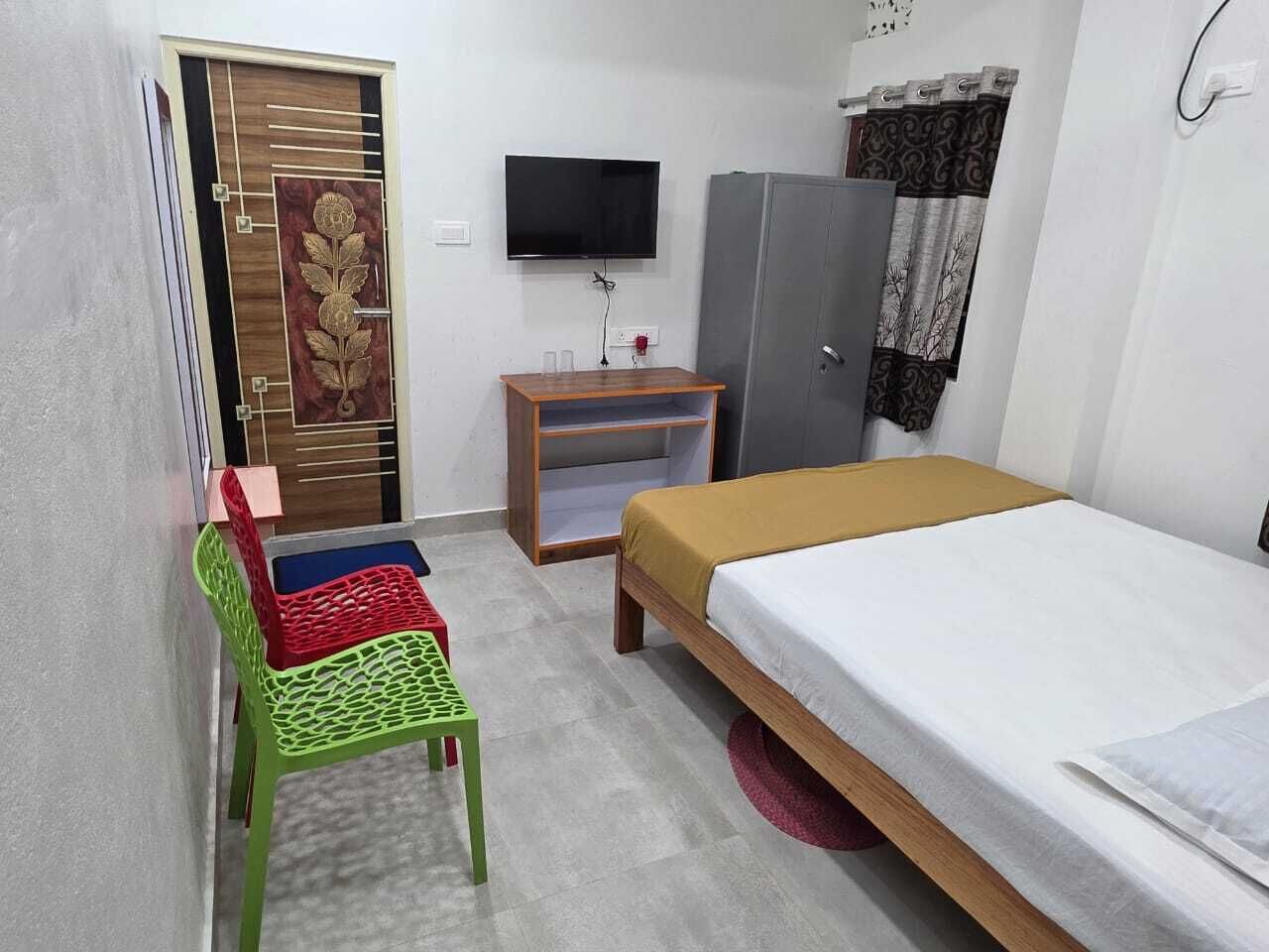 A room with a bed, a TV mounted on the wall, a wardrobe, and a chair.