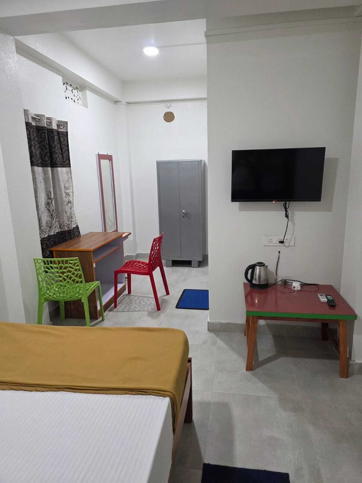 A hotel room with a bed, a desk, a television, a wardrobe, and a red chair.
