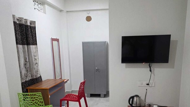 A hotel room with a bed, a desk, a television, a wardrobe, and a red chair.