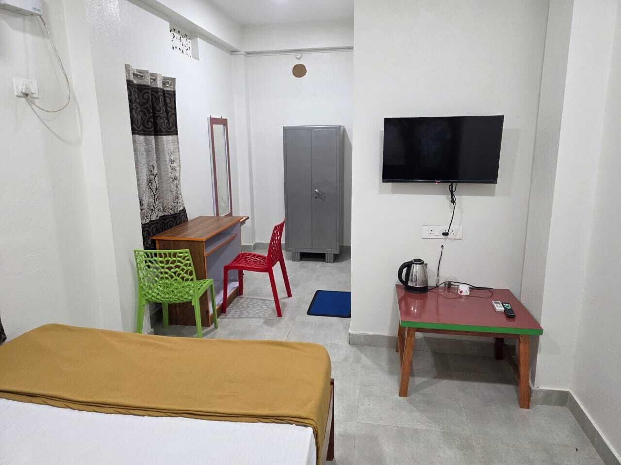 Um quarto com cama, escrivaninha, televisão e guarda-roupa.