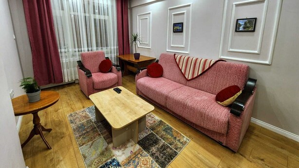 Ein Wohnzimmer mit einer Couch, zwei Sesseln, einem Couchtisch, einem kleinen Beistelltisch und einer Topfpflanze.