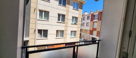 Un balcon avec une balustrade en métal, une vue sur des immeubles à plusieurs étages et un ciel bleu dégagé.