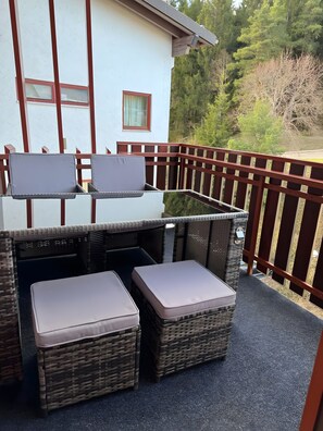 Un balcone con mobili in vimini, un edificio bianco con finestre e una recinzione in legno.