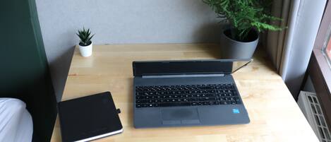 A laptop on a wooden desk with a potted plant and a notebook beside it.