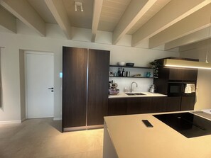 A modern kitchen with a built-in oven, a sink, and a countertop with a phone. There is a door and a shelf with kitchen items. - Villa Carmel (Tremezzo)