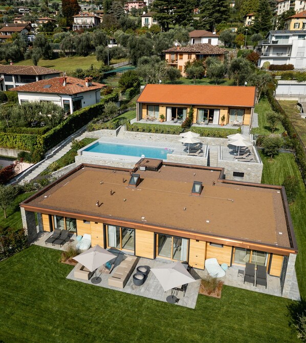 Una casa moderna con piscina, un patio con mobiliario exterior y un jardín bien cuidado.