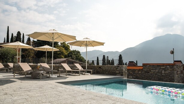A pool area with lounge chairs and umbrellas, surrounded by stone walls and a mountainous backdrop. - Villa Carmel (Tremezzo)