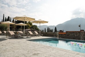 Zona de piscina con sillones de descanso y sombrillas, rodeada de muros de piedra y un paisaje montañoso.
