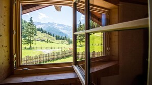Una cabaña de madera con un ventanal grande que ofrece vistas a un valle verde y montañas.