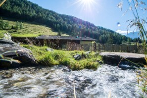 Una casa vicino a un ruscello, con un recinto in legno e montagne sullo sfondo.