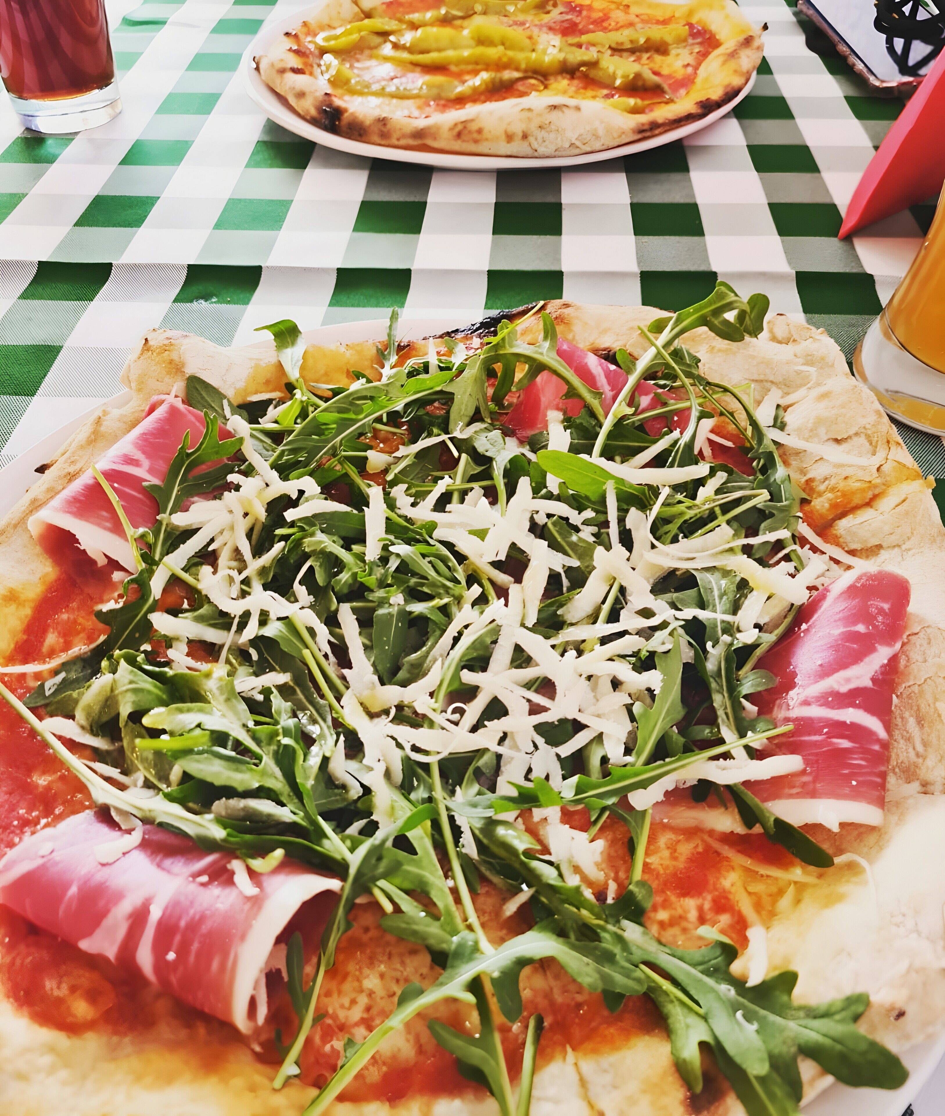 Pizza con rúcula y prosciutto sobre un mantel a cuadros verde y blanco.